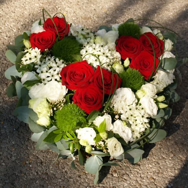 Corazón funerario con rosas rojas, flores blancas y follaje verde, diseñado por Floristería Sayde en Zaragoza. Arreglo floral para funerales y despedidas.