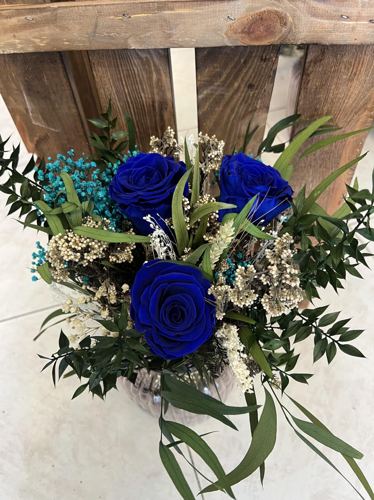 Ramo Preservado de Rosas Azules con follaje verde, flores secas en tonos crema y turquesa, acompañado de un jarrón decorativo de vidrio. Creación exclusiva de Floristería Sayde, Zaragoza.